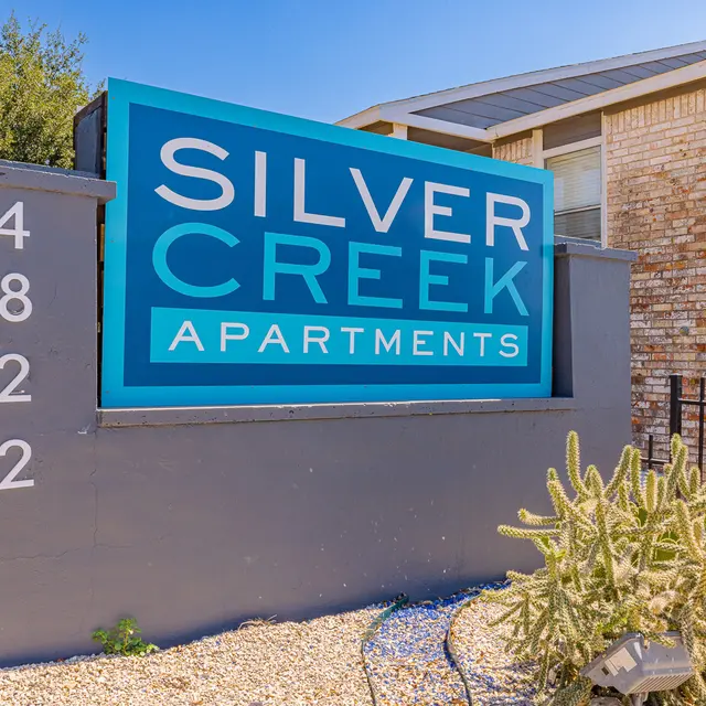 Sign for Silver Creek Apartments, featuring the text 'Silver Creek Apartments' on a blue background, surrounded by landscaping including cacti.