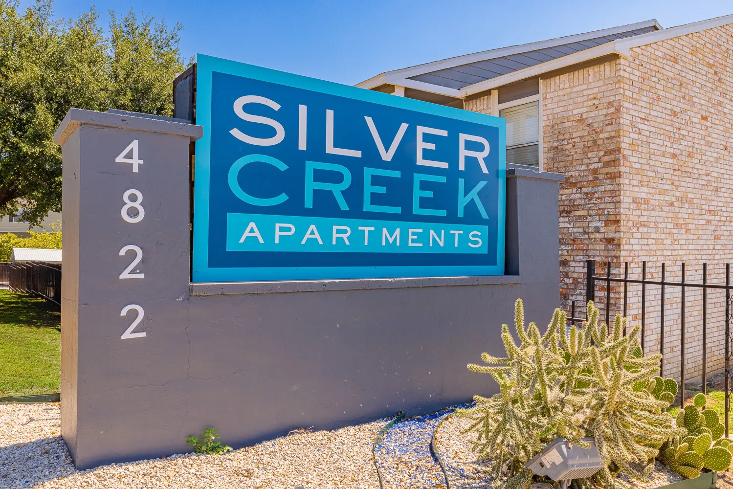 Sign for Silver Creek Apartments, featuring the text 'Silver Creek Apartments' on a blue background, surrounded by landscaping including cacti.