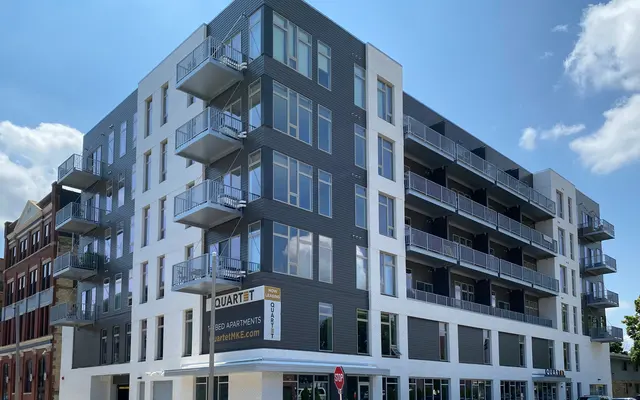 Modern multi-story apartment building with balconies under a blue sky with clouds.
