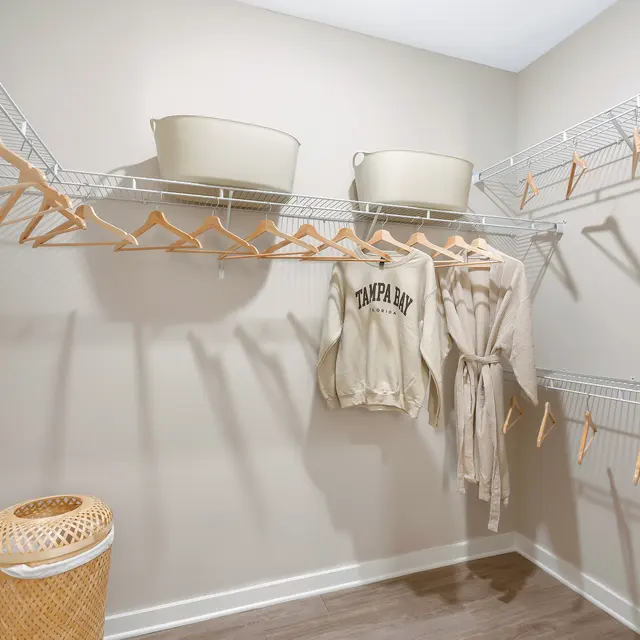 Modern Closet Interior A spacious closet with wire shelving, featuring several hangers, a light-colored robe, a grey sweatshirt, storage bins, and a woven laundry basket on the floor.