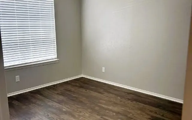 Empty room with light gray walls, a laminated wooden floor, and a window with blinds. Simple and spacious interior.