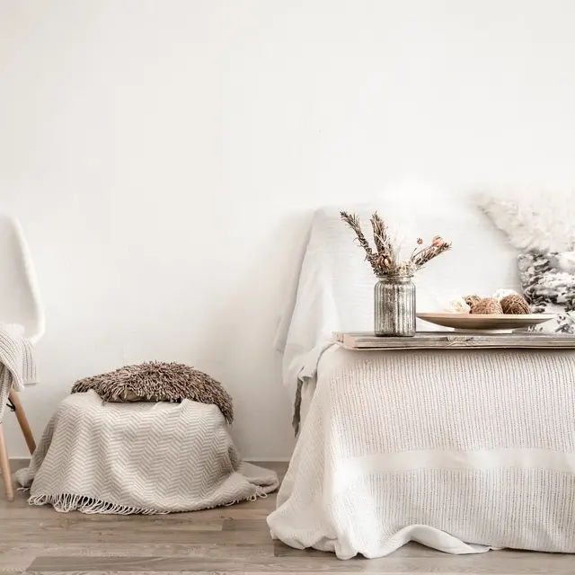 Cozy living space featuring a minimalist design with neutral tones, a plush blanket, and decorative elements on a table.