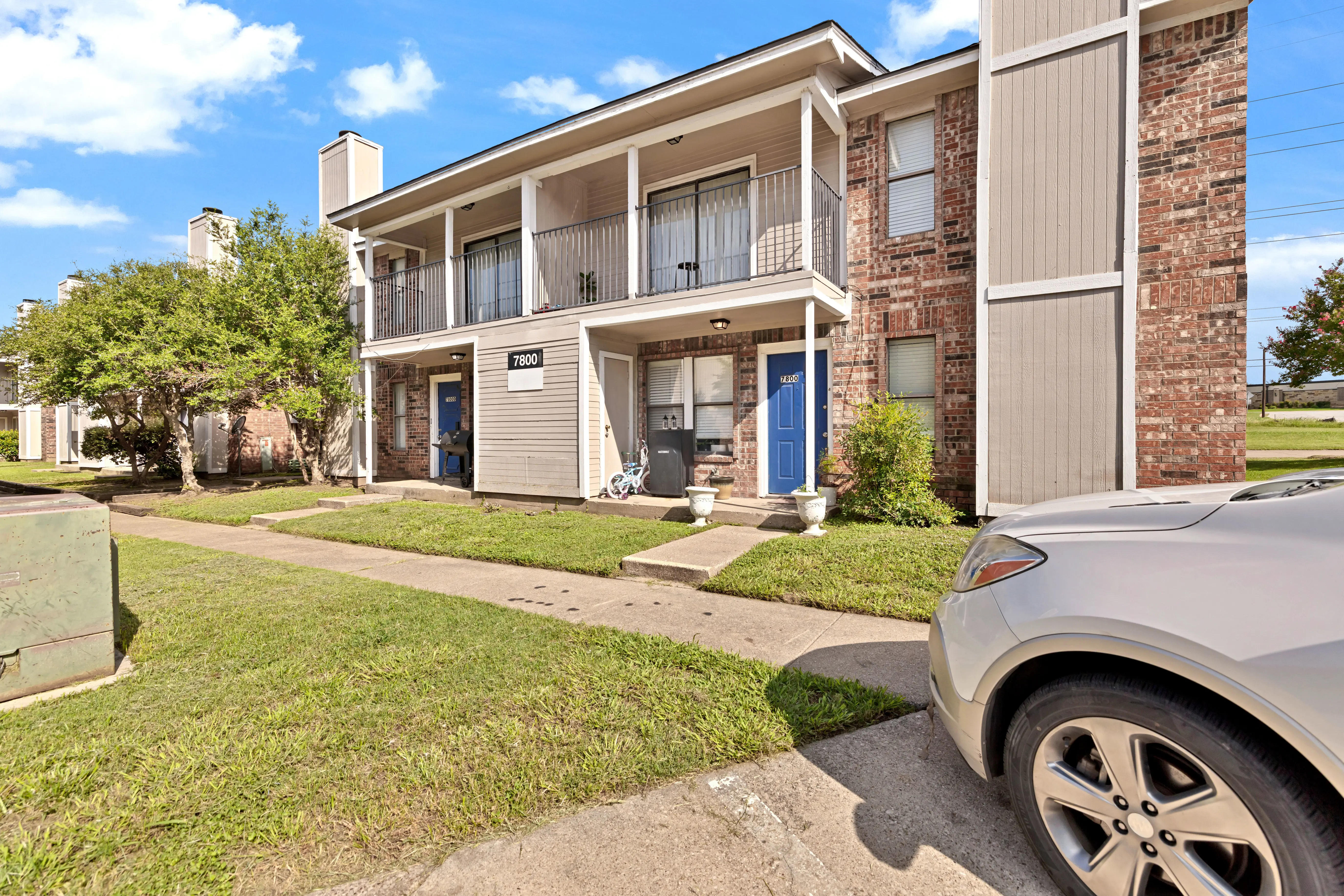 Exterior view of a two-story apartment building with a green lawn and parked car in front.