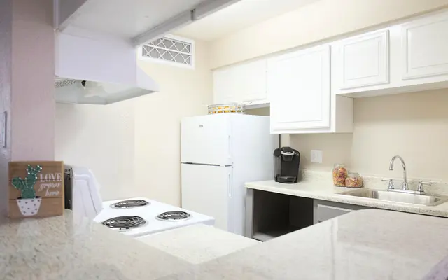 A modern and clean kitchen showcasing a white refrigerator, stove, and sink with granite countertops.