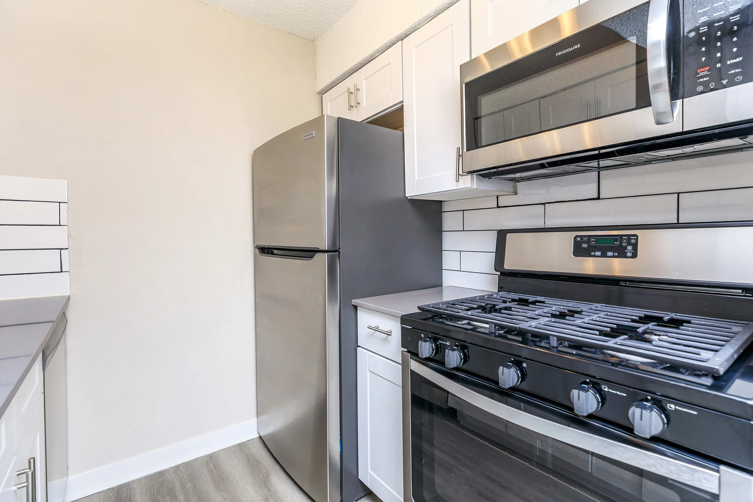 Kitchen with sink, countertop, black steel appliances with a white tile backsplash and cabinets. 