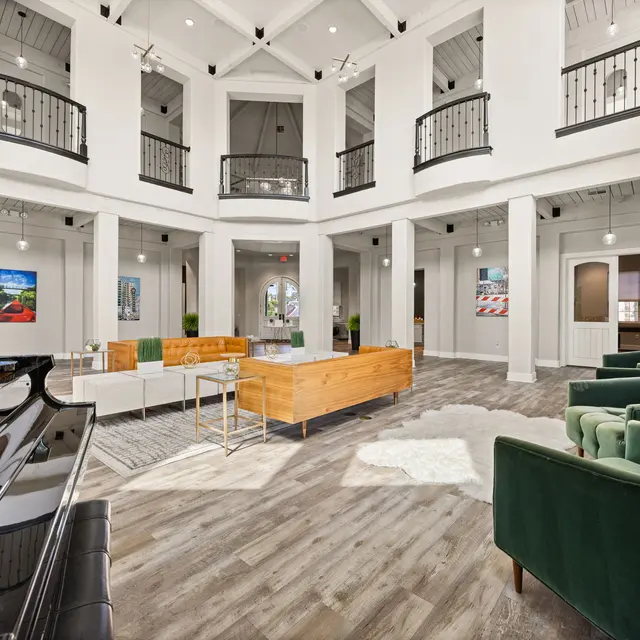 Modern Living Area Interior A spacious and modern living area with high ceilings, large windows, and stylish furniture. The room features a black piano, green velvet chairs, and wooden coffee tables surrounded by art pieces.