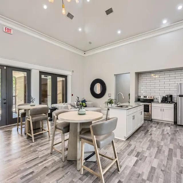 A modern kitchen and lounge area featuring a dining table with four chairs, a stylish kitchen with stainless steel appliances, large windows letting in natural light, and contemporary decor.