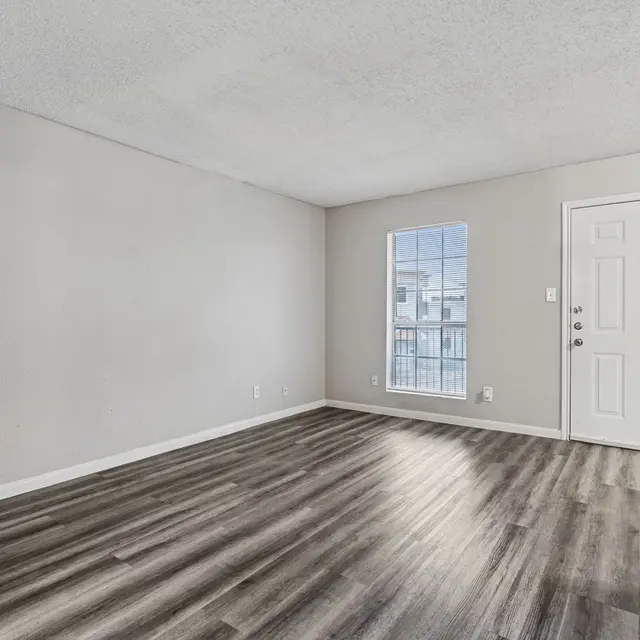 Empty living room with light gray walls and dark wood-like flooring.