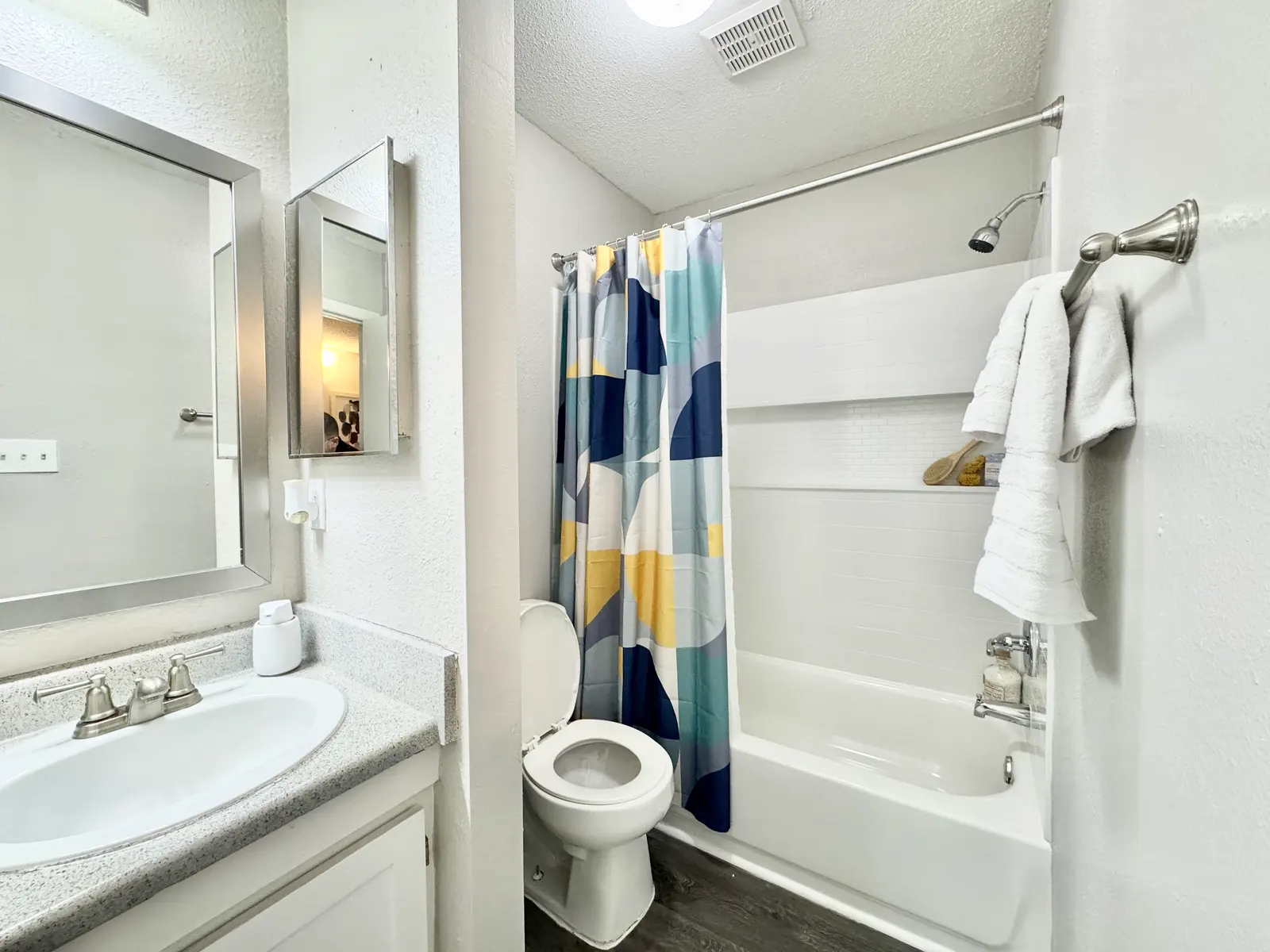 A modern bathroom with a shower and bathtub, featuring a colorful shower curtain, a white toilet, and a large mirror above the sink.