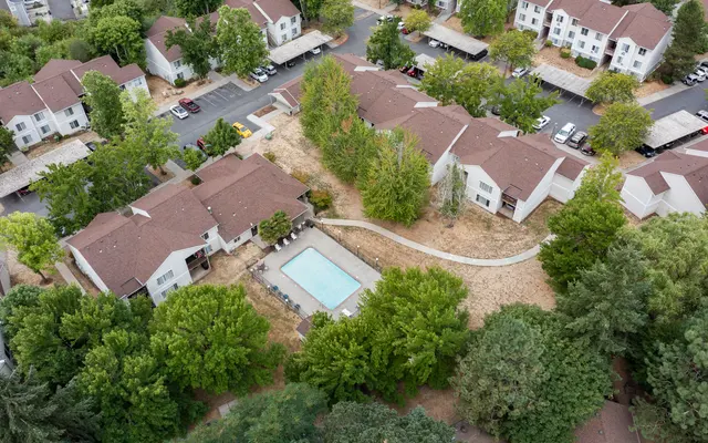 Aerial view of a residential apartment complex with brown rooftops and a central swimming pool surrounded by greenery.