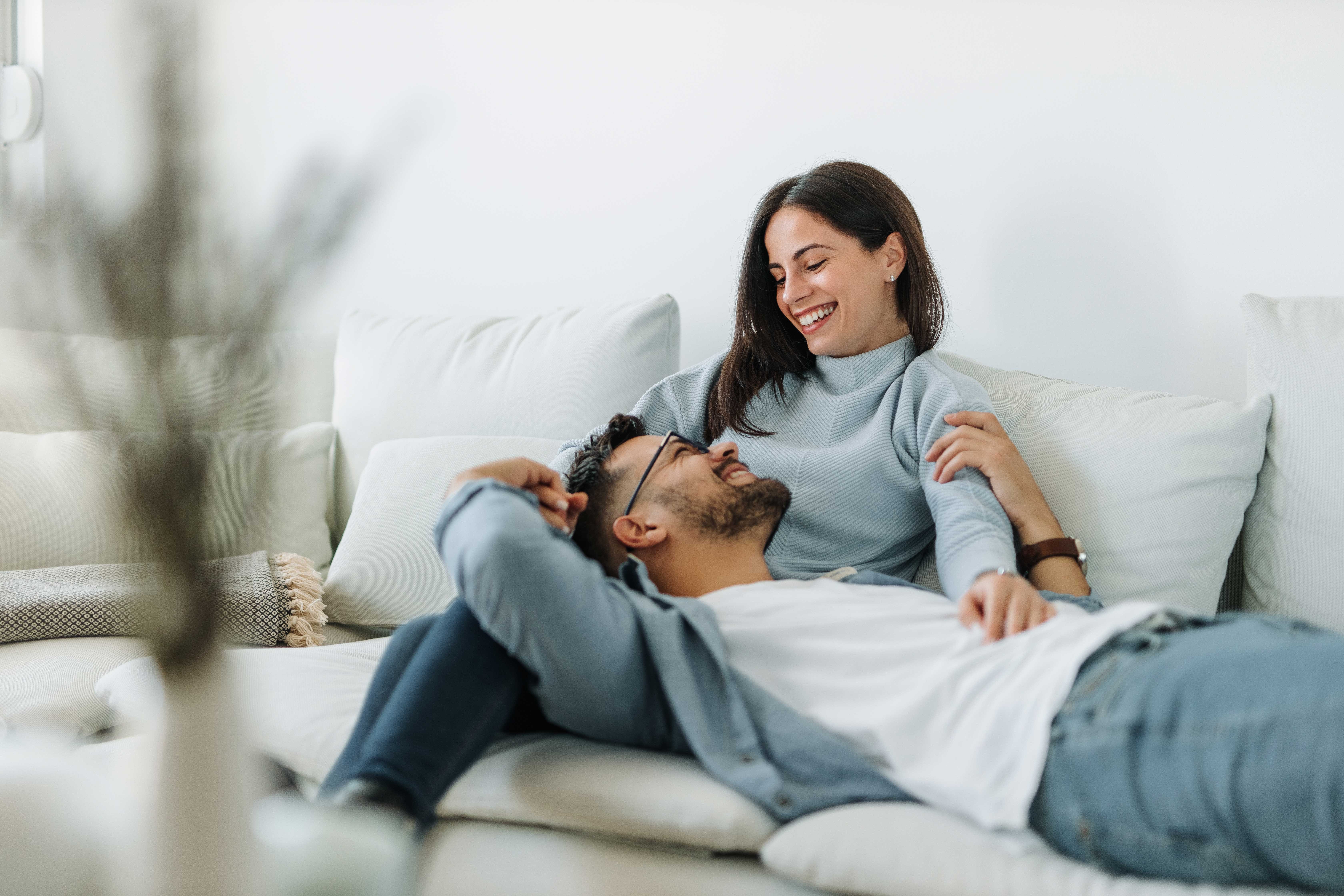 Loving Moment on the Couch A couple enjoying a moment together on a couch. The woman is smiling while sitting closely to the man, who is lying down, looking up at her.