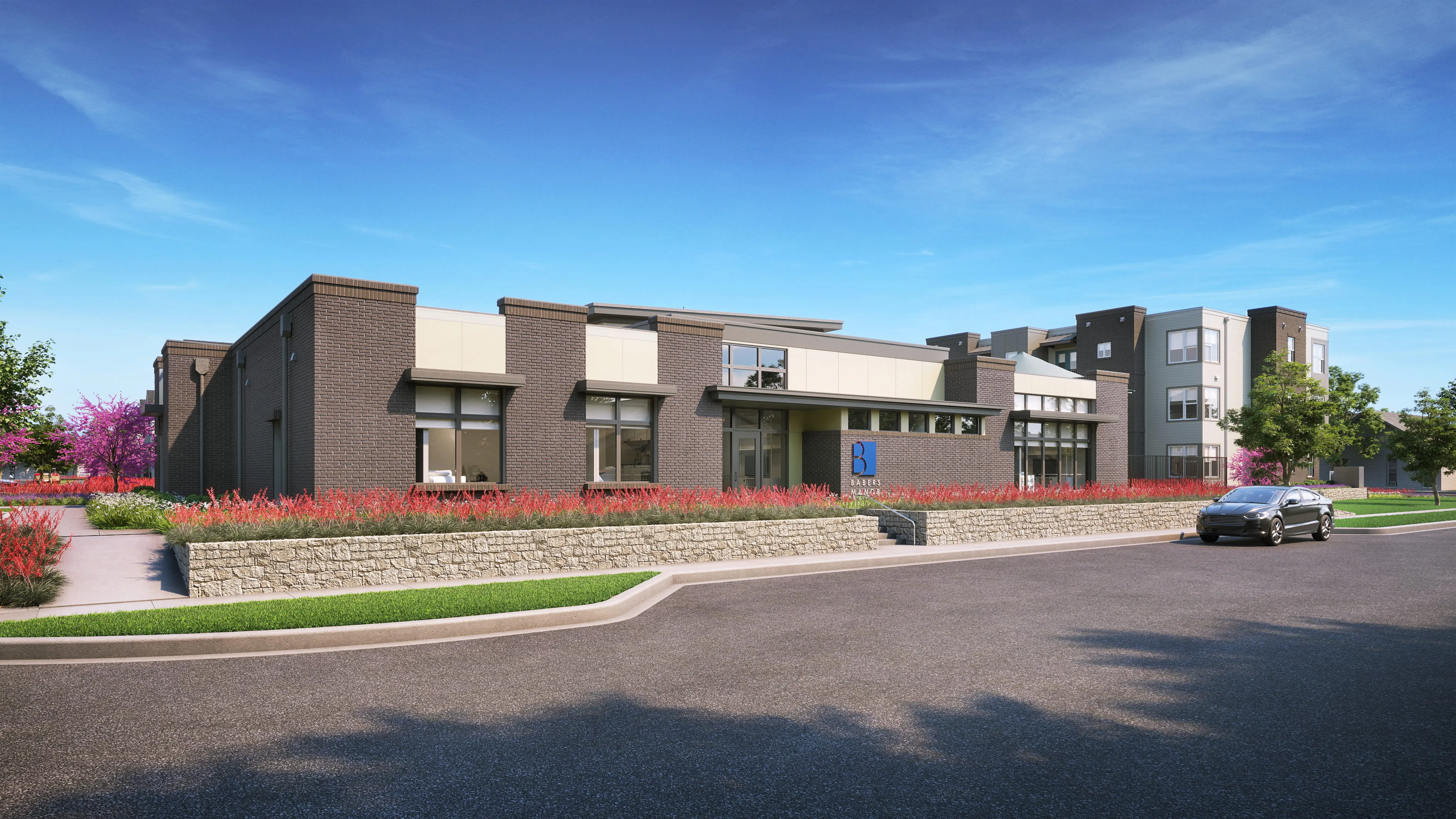 Modern Building Frontage A modern building facade with landscaped gardens in front, featuring shrubs and flowers, situated along a paved road under a clear blue sky.