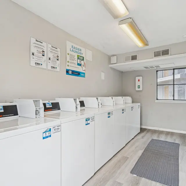 A clean and organized laundry room featuring several washing machines and dryers along one wall.