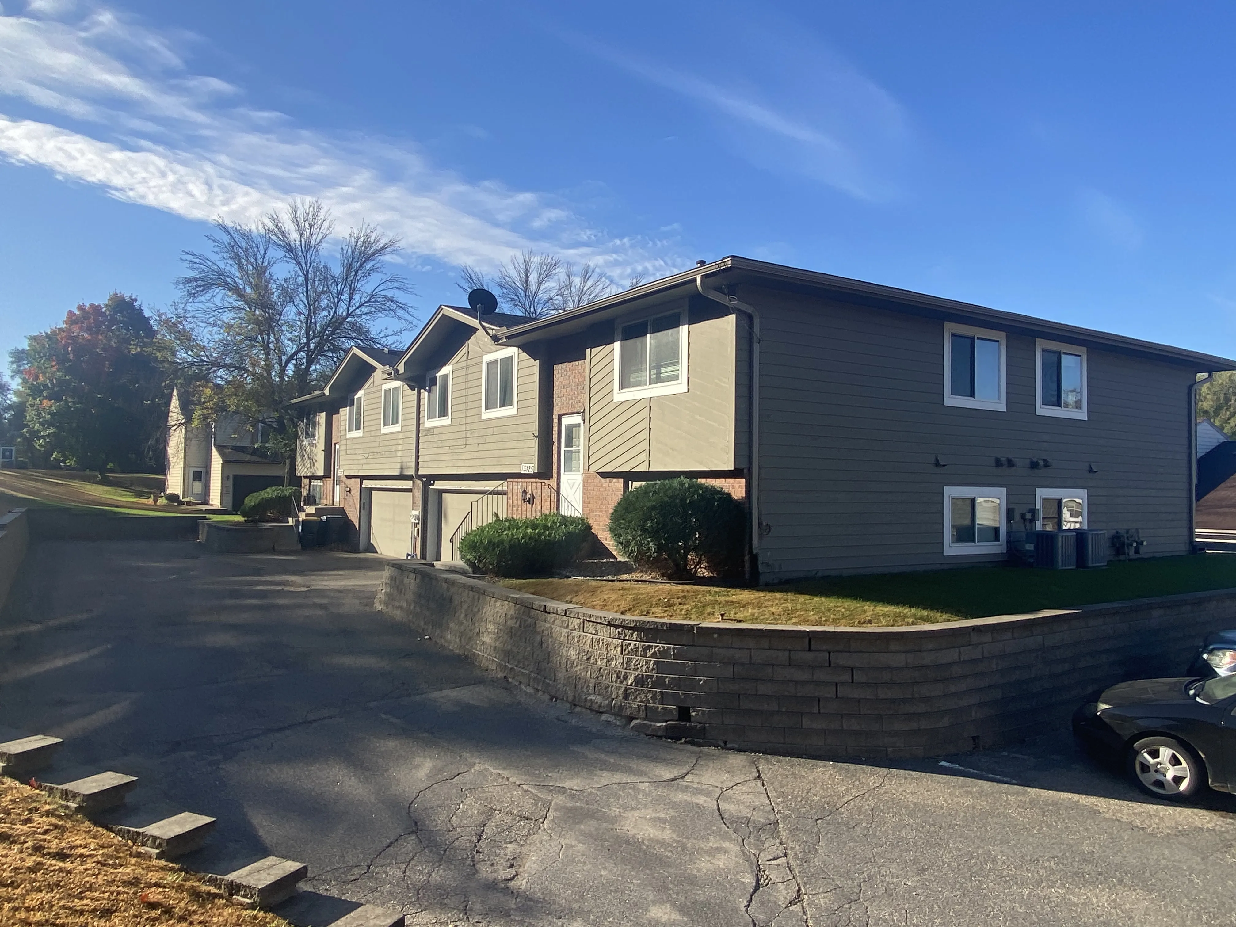 Court Place - Exterior View of a row of two-story apartment buildings, with a paved driveway leading up to them. Green grass and trees are visible in the background, under a clear blue sky.