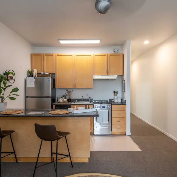 A modern kitchen area featuring wooden cabinets, stainless steel appliances, and a small dining space with two high stools.