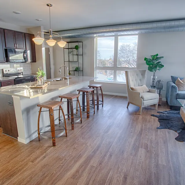 Modern kitchen and living space at Woodrow Apartments in Fargo with island seating, light wood floors, and natural lighting