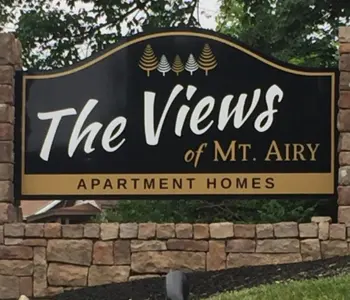 Sign for The Views of Mt. Airy Apartment Homes with stone background and green foliage