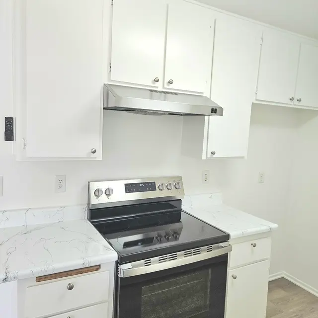A clean and modern kitchen featuring white cabinetry, a stainless steel stove, and a marble countertop.