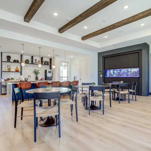 A modern indoor dining area featuring wooden beams on the ceiling, a variety of tables and chairs, and an aquarium wall with a cozy aesthetic.