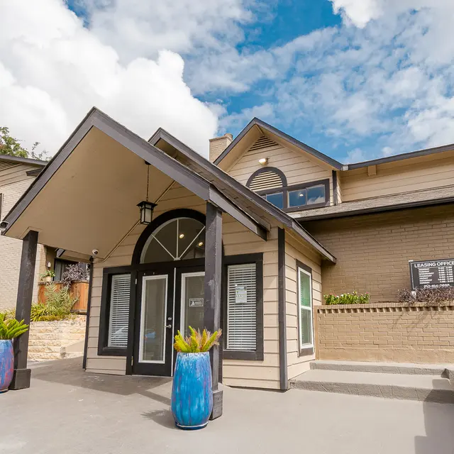 Exterior view of an apartment complex entrance featuring large doors, a covered entryway, and decorative plants.