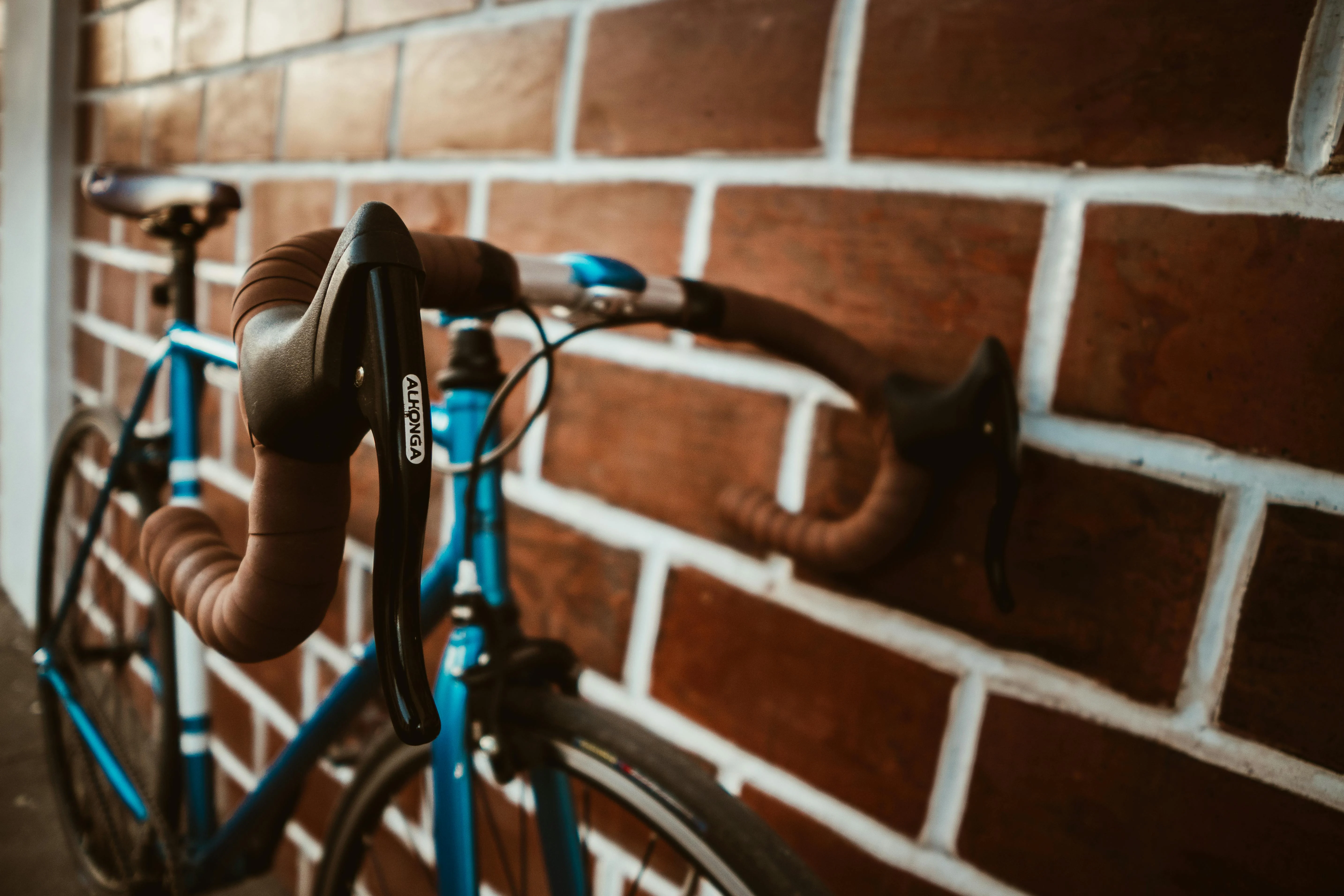 A close-up view of a blue bicycle's handlebar against a brick wall.