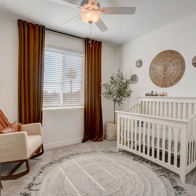 Charming Nursery Interior A well-decorated nursery featuring a white crib, a cozy armchair, a round rug, and decorative wall hangings. Natural light comes through a window with dark curtains.