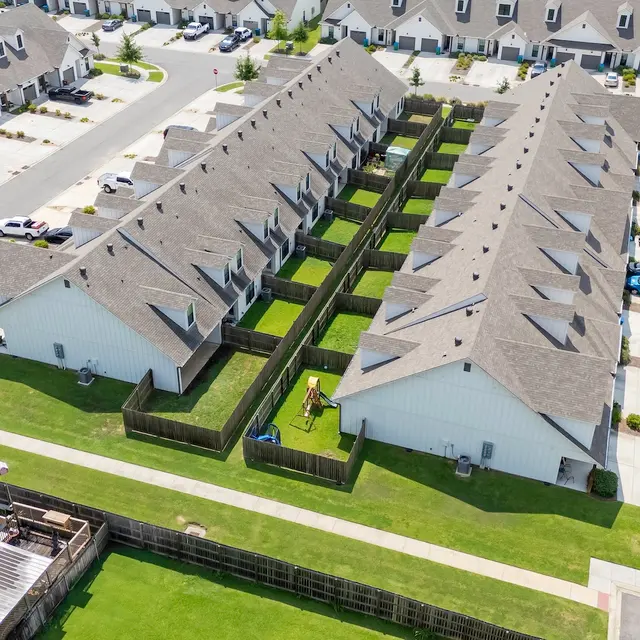 Residential Complex Aerial View Aerial view of a residential area with several townhouses arranged in rows, featuring well-manicured lawns and parking spaces.