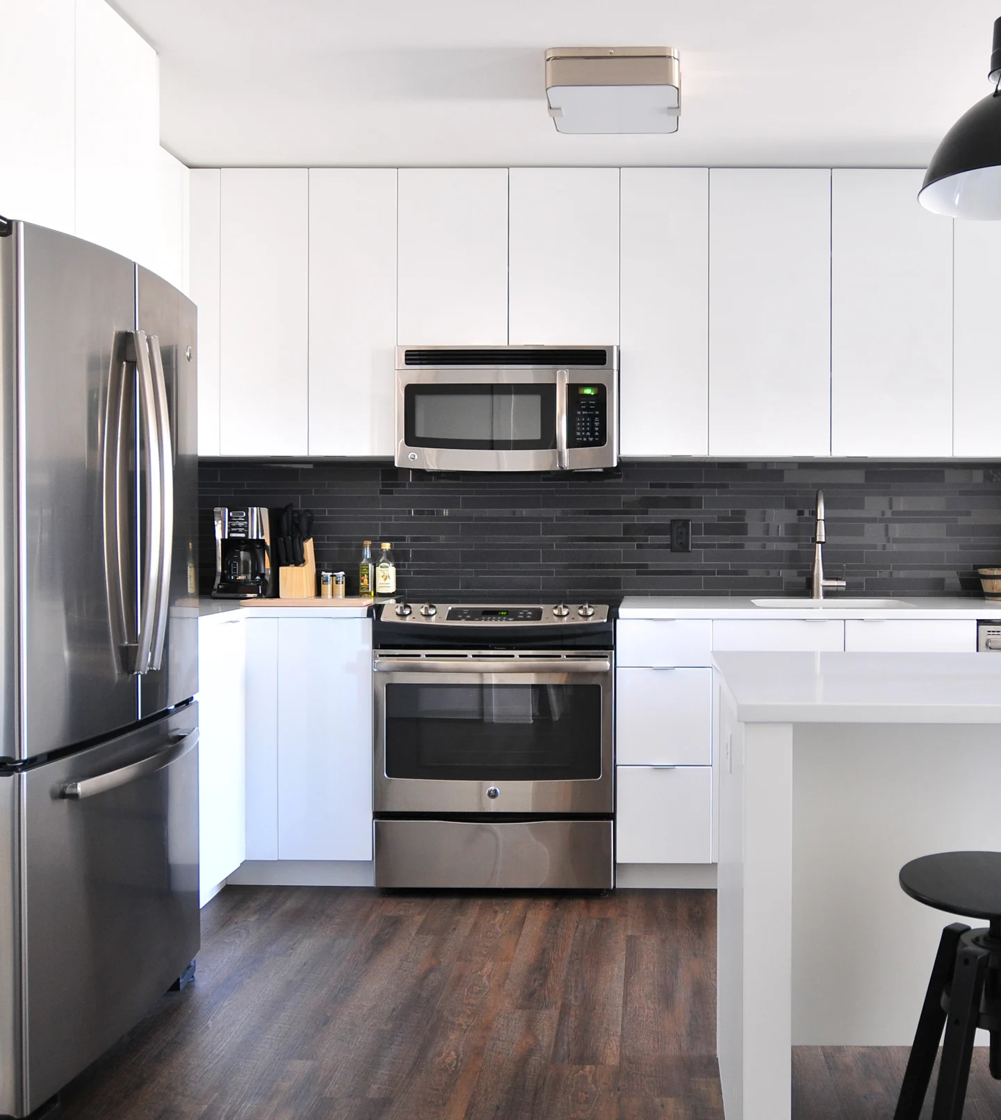 Modern kitchen featuring stainless steel appliances, white cabinets, and a dark backsplash, with a minimalist design.