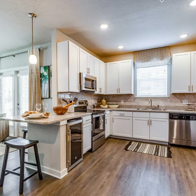 ShoreView A U-shaped kitchen with a window, cabinets, a wine cooler, and stainless steel appliances near a living room with patio doors.