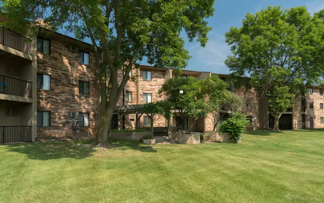 an exterior photo of The Woods of Burnsville's apartment buildings with trees and a luscious green lawn - Grass, Plant, Lawn