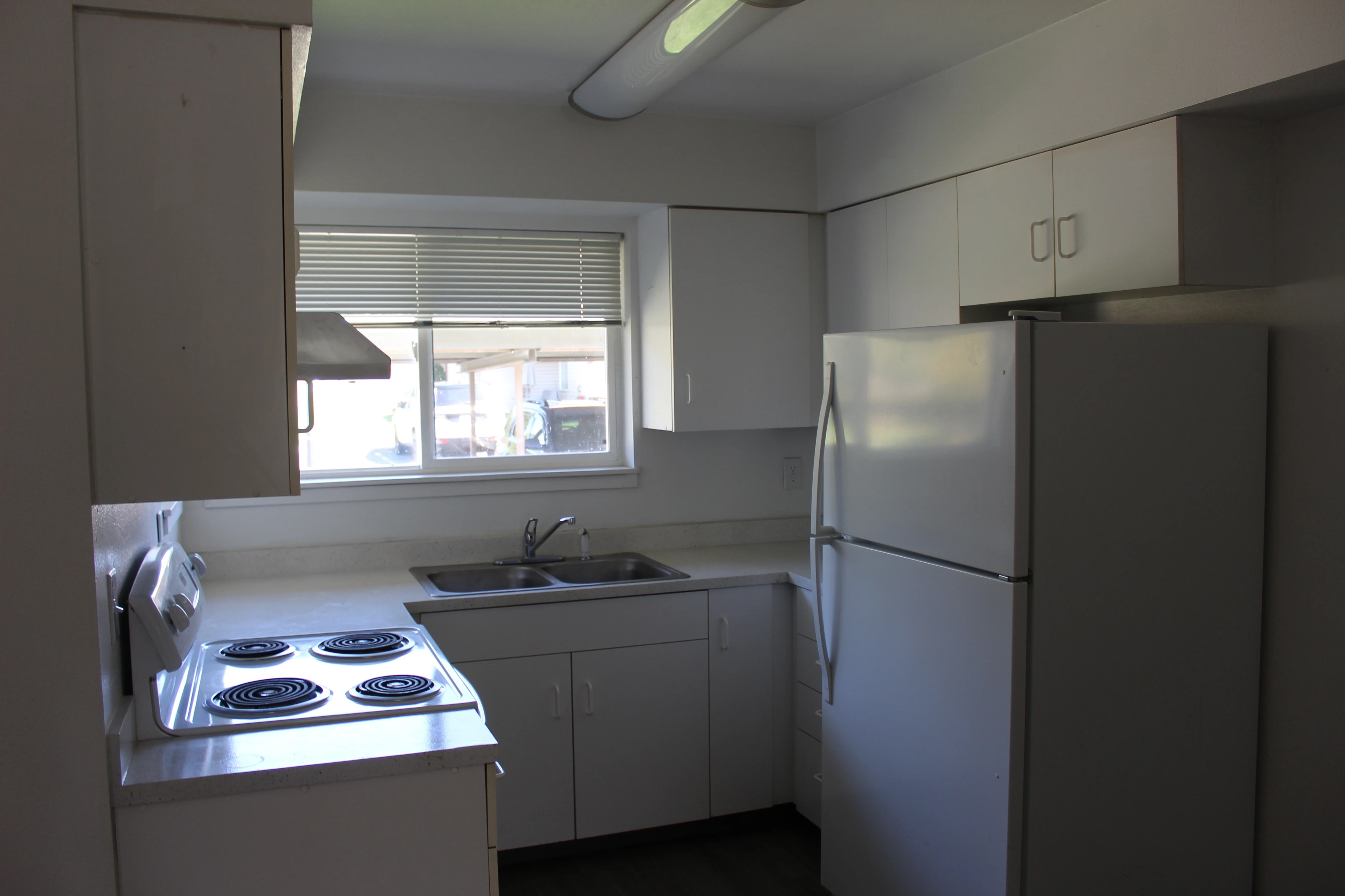 A kitchen featuring a stove, refrigerator, sink, and white cabinets, with a window providing natural light.