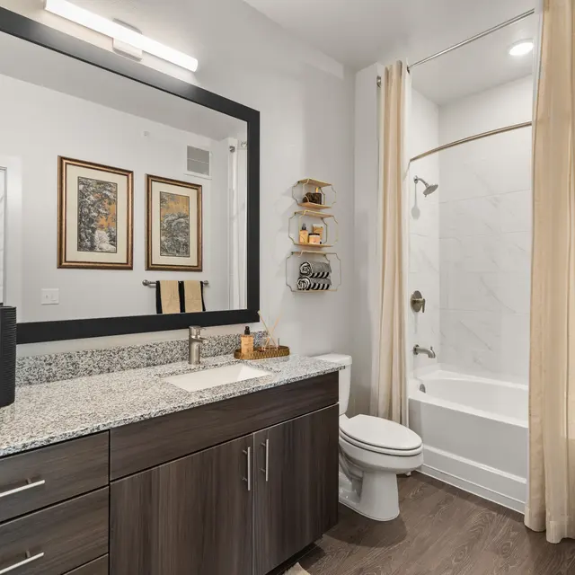 Modern Bathroom Interior A modern bathroom featuring dark wooden cabinetry, a large mirror, and beige drapes. The bathroom includes a bathtub with a shower and decorative wall art.