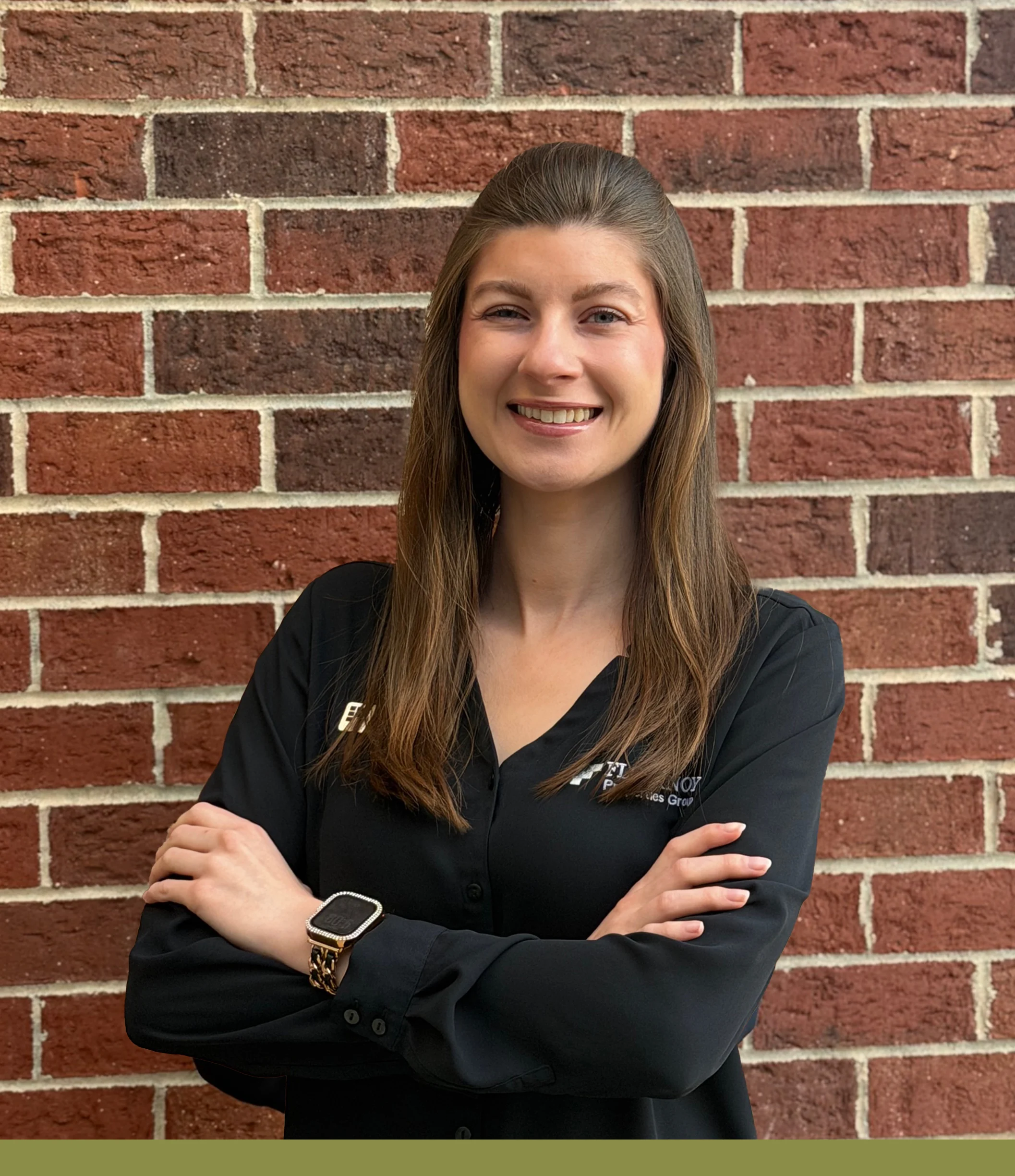 Professional Headshot A smiling woman with long hair wearing a black button-up shirt, standing with her arms crossed against a brick wall.