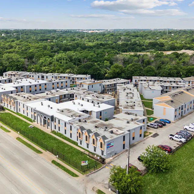 Aerial view of a large multi-building apartment complex situated near a road, surrounded by greenery and trees.