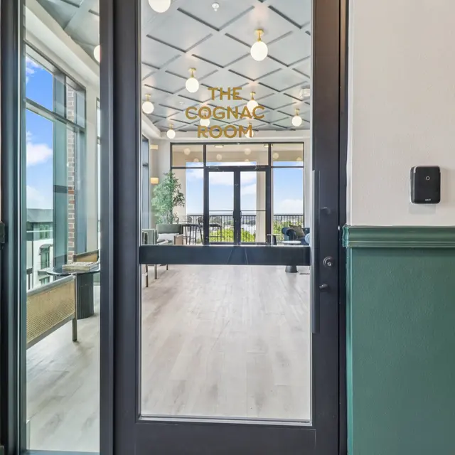 A modern entryway to a room with glass doors featuring a sign that reads 'The Cognac Room'. The interior shows a well-lit space with large windows and a view, along with stylish decor.