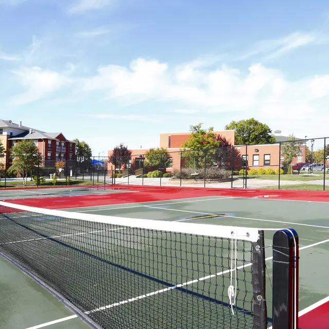 Outdoor Tennis Courts View of multiple tennis courts with red and green surfaces, surrounded by trees and buildings, under a clear blue sky.
