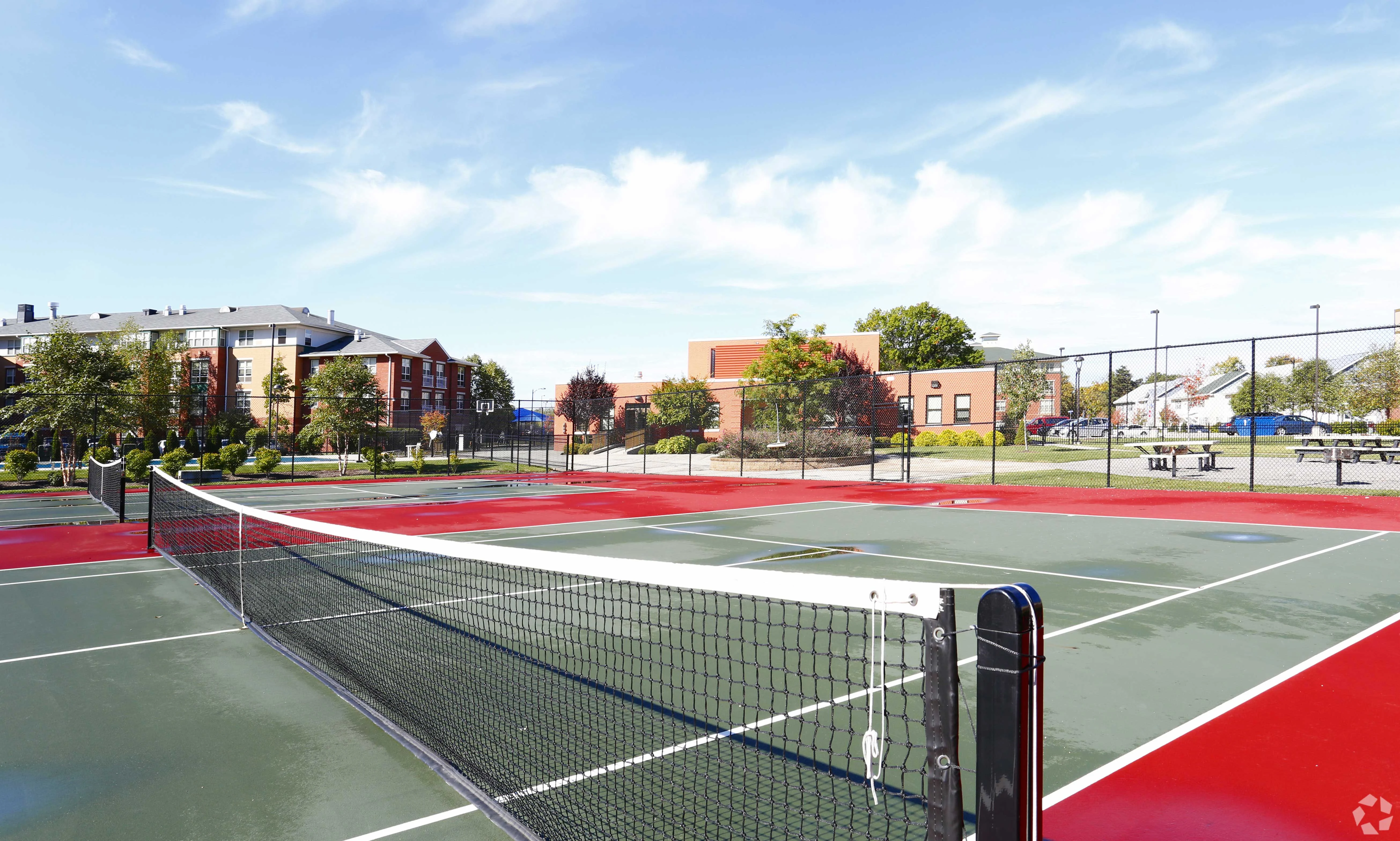 Outdoor Tennis Courts View of multiple tennis courts with red and green surfaces, surrounded by trees and buildings, under a clear blue sky.