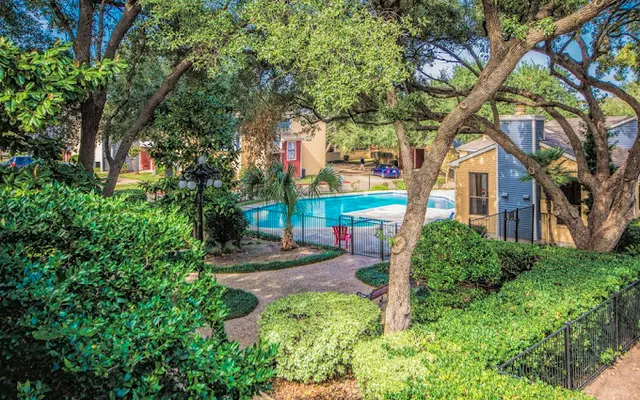 A serene view of a swimming pool surrounded by lush greenery and trees in an apartment complex.