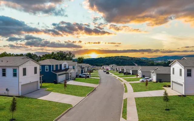 A quiet suburban neighborhood with houses on either side of a street, showcasing a beautiful sunset with colorful clouds above the horizon.