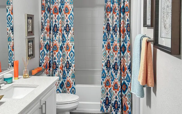 A stylish bathroom featuring colorful patterned curtains, a white vanity with a sink, a toilet, and a decorated rug on the floor.
