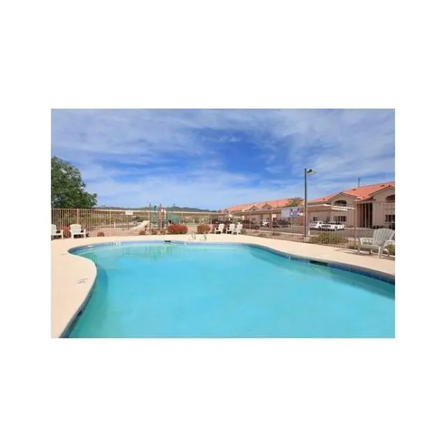 Swimming Pool Area A clear blue swimming pool surrounded by a patio with lounge chairs. There are several buildings in the background against a partly cloudy sky.