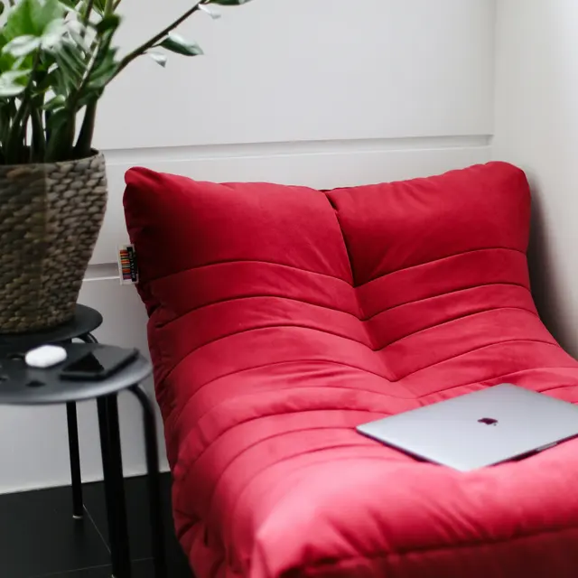 A cozy red bean bag chair next to a small black table and a green plant in a pot.