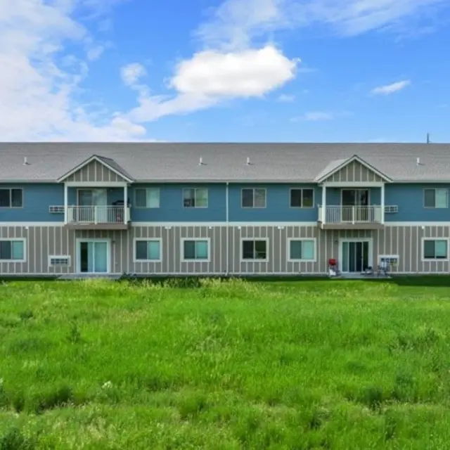 Granite Peak A two-story apartment building with a mix of blue and beige siding, surrounded by a green lawn under a blue sky with some clouds.