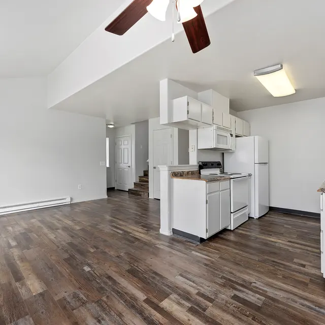 Spacious Modern Apartment Interior A spacious and modern kitchen-living area featuring wooden floors, white cabinets, and appliances. A ceiling fan is visible above.