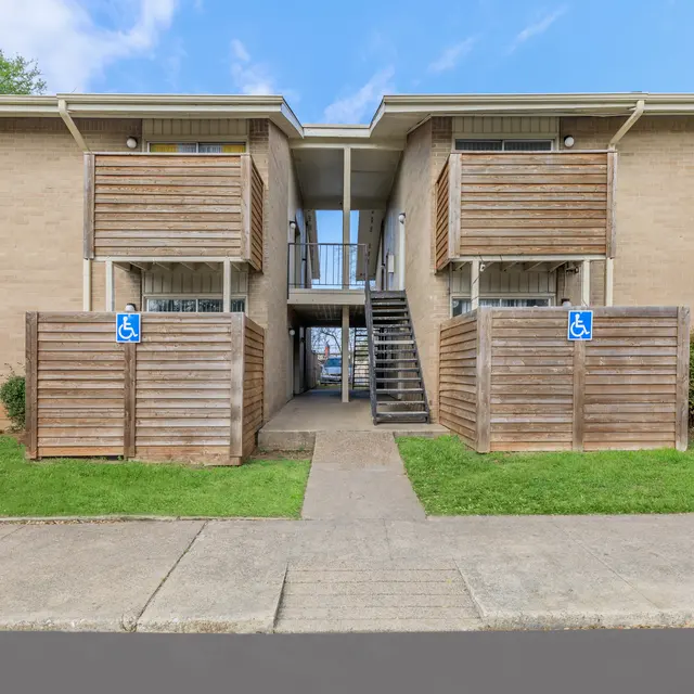 Apartment Complex Entrance Entrance of a two-story apartment complex with wooden balcony enclosures and a concrete pathway leading to the stairs.