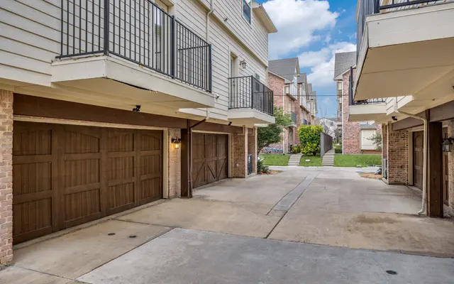Residential Parking Area with Garages View of a parking area featuring multiple garages beneath residential units, with green space visible in the background.