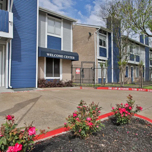 Exterior view of an apartment complex featuring a Welcome Center and landscaped area with flowers.