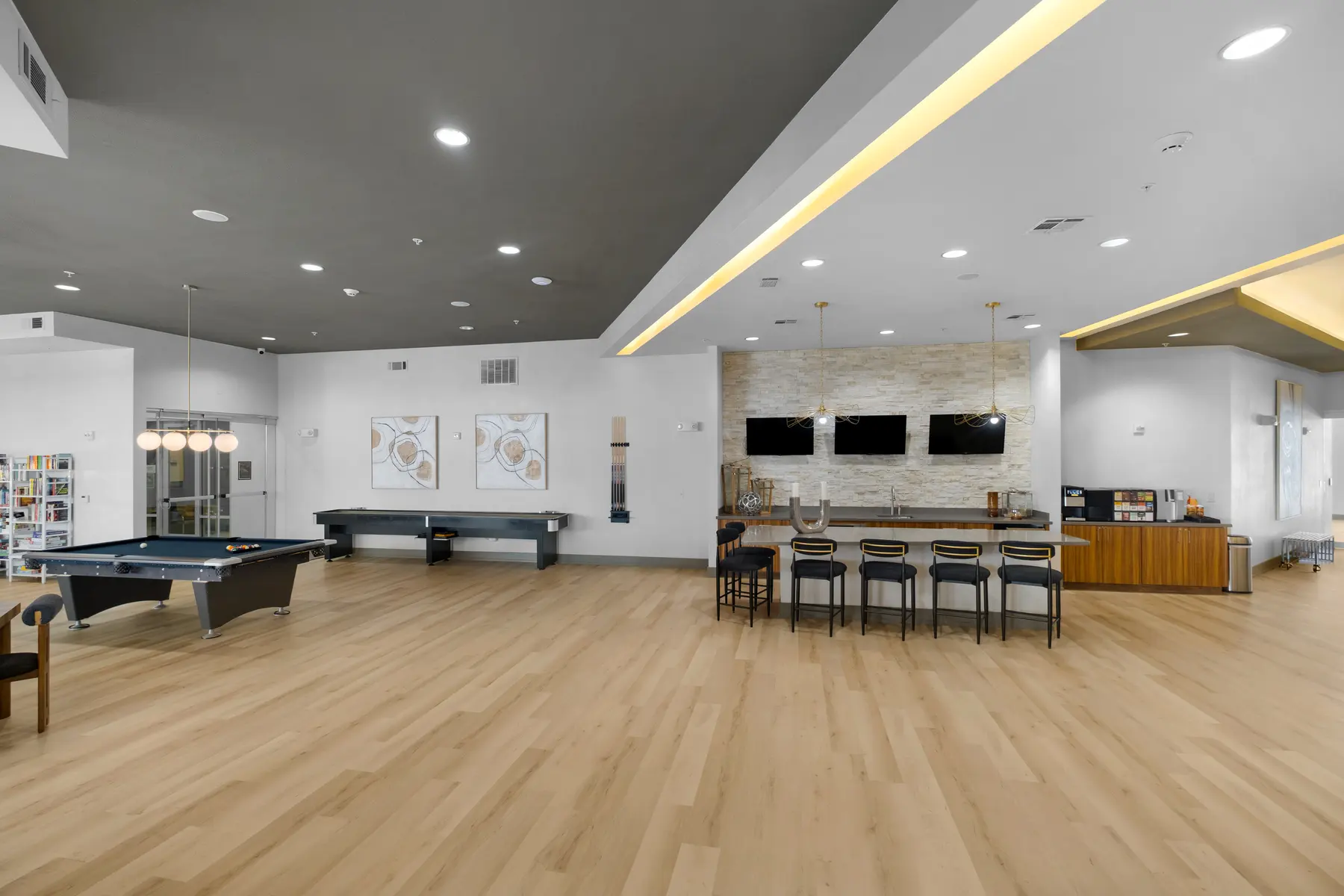 A spacious community lounge featuring a game table, seating area, and a bar counter with several stools.