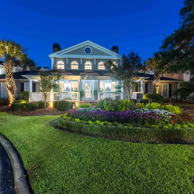 A beautifully lit building at night with a large flower bed in the foreground and palm trees on the side.