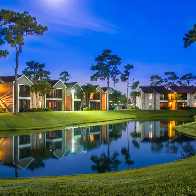 Venice Park lakefront apartments at night time with glowing lights and lush greenery.